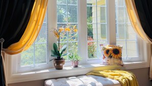 Una habitación con un banco junto a la ventana, una planta en maceta y una almohada con girasol.