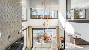 A modern interior with a dining area, a sofa, and a view of the outdoors. - Villa El Paraiso | Cinema Gym Pool Parking (Benahavís)
