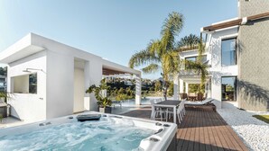 A modern outdoor hot tub area with a wooden deck, white walls, and a view of a residential neighborhood. - Villa El Paraiso | Cinema Gym Pool Parking (Benahavís)