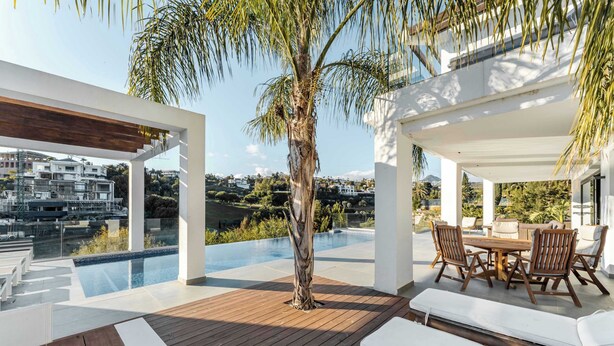 A modern outdoor deck with a wooden floor, a pool, and a dining area with chairs and a table. - Villa El Paraiso | Cinema Gym Pool Parking (Benahavís)