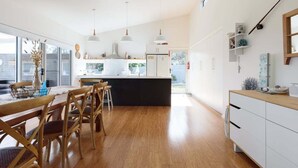 A modern kitchen with a central island, pendant lighting, and a dining area with wooden chairs. - Low Head Coastal Haven: Your Seaside Escape (George Town)
