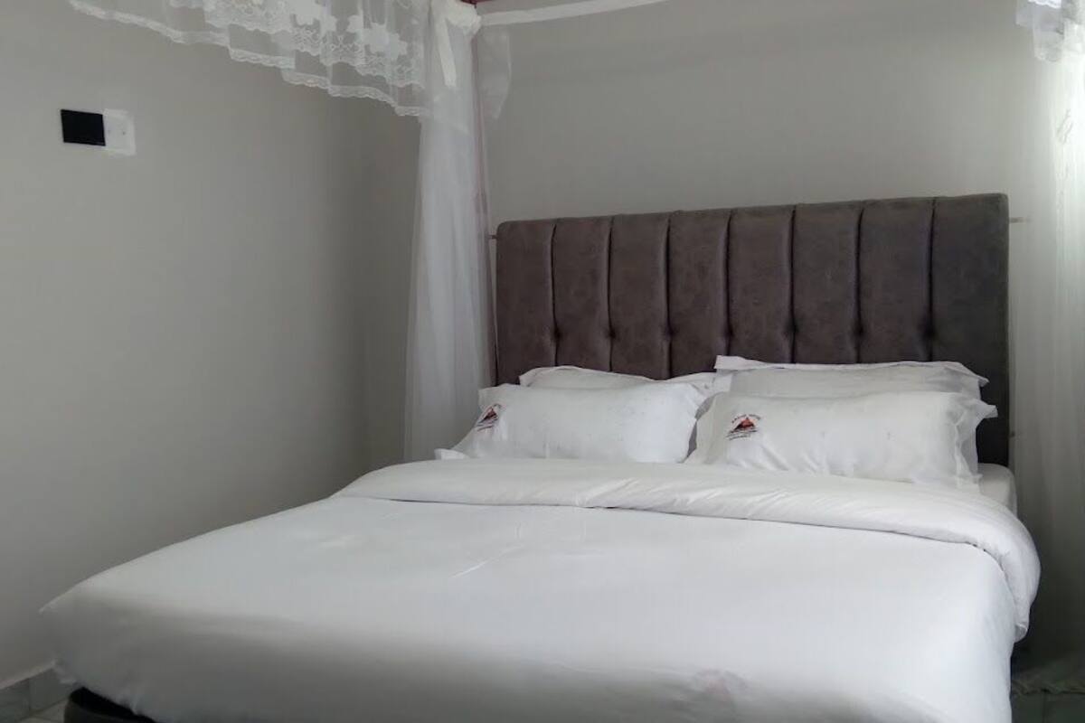 A neatly made bed with white linens and a brown headboard in a room with white walls.