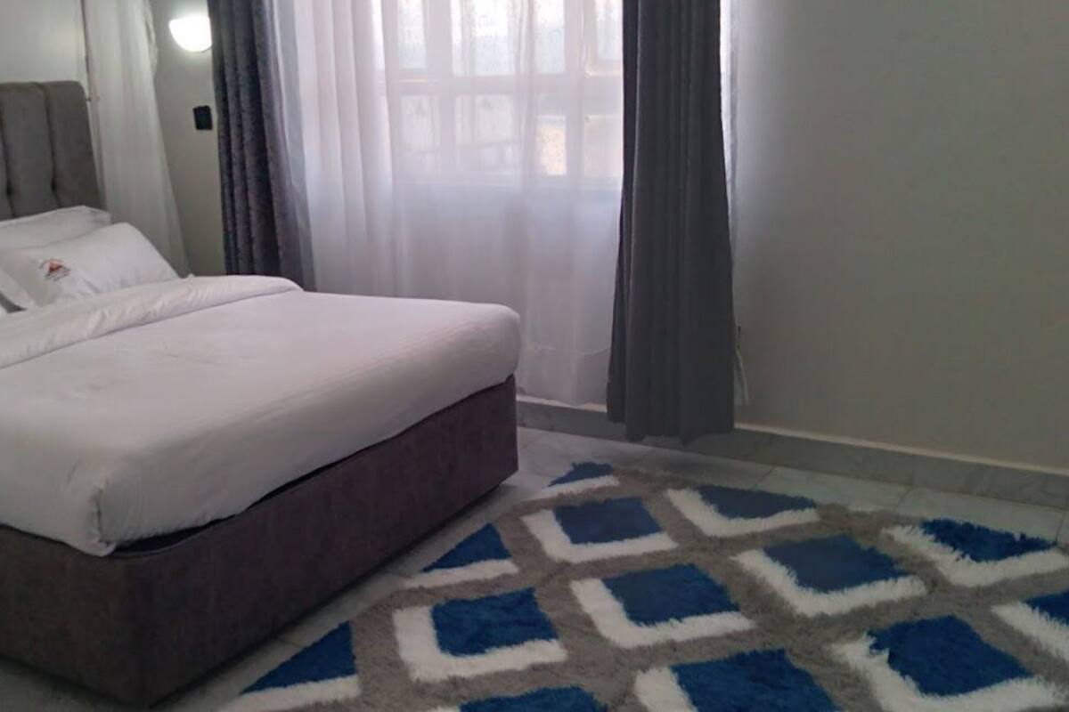 A bedroom with a bed, a patterned rug, and curtains.