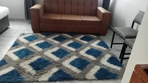 A room with a brown sofa, a blue and white checkered rug, a grey chair, and a bed with white bedding. - Saimo Hotel Kabarnet (Kabarnet)