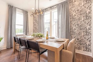 A dining area with a wooden table set for four, black chairs, and a chandelier. - Summer rooftop fire pit, skyline views, garage near Broadway (Nashville)