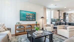 Een moderne woonkamer met een flatscreen televisie, een houten salontafel en een console. In de achtergrond is een keuken te zien.