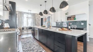 Een moderne keuken met donkere kastjes, een groot eiland, hanglampen en uitzicht op de eethoek.