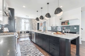 A modern kitchen with dark cabinetry, a large island, pendant lighting, and a view to the dining area.