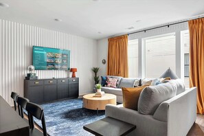 A modern living room with a grey sofa, a round coffee table, and a TV mounted on the wall. - Hot tub Nashville home for families • 3BR sleeps 10 near Broadway (Nashville)