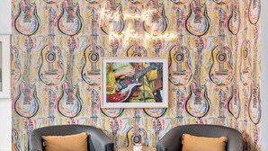 A room with a vibrant guitar pattern wallpaper, two black leather chairs with tan cushions, a small round table with a black base, and a framed picture of a guitar player.