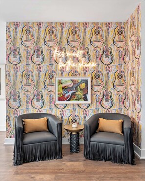 A room with a vibrant guitar pattern wallpaper, two black leather chairs with tan cushions, a small round table with a black base, and a framed picture of a guitar player. - Nashville hot tub retreat near Germantown, sleeps 10 in 3 bedrooms (Nashville)