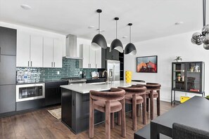 A modern kitchen with a central island, bar stools, pendant lighting, and a dining area with a table. - Hot tub Nashville home for families • 3BR sleeps 10 near Broadway (Nashville)