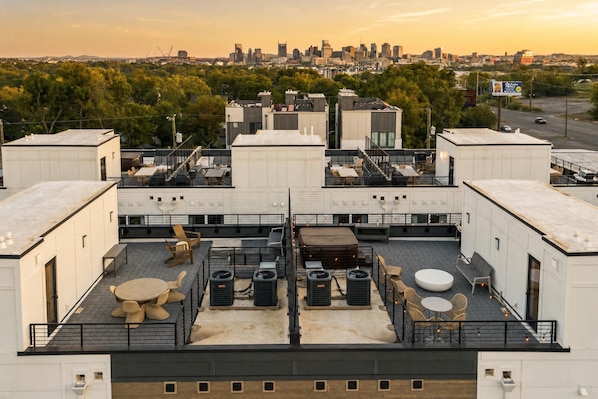 Terraço no telhado com área de estar externa, aparelhos de ar condicionado e vista para o horizonte da cidade ao fundo.