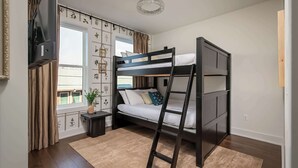 A bunk bed room with a TV, a small table, a plant, and a window with curtains.