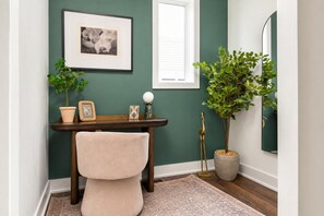 Una habitación con escritorio, una silla, una planta en maceta, un cuadro enmarcado y un espejo.