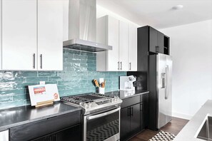A modern kitchen with a gas stove, oven, black cabinets, and a stainless steel refrigerator.