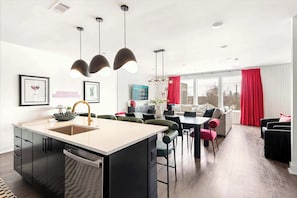 A modern kitchen with a central island, a dining area with chairs, a sofa, and a red curtain.