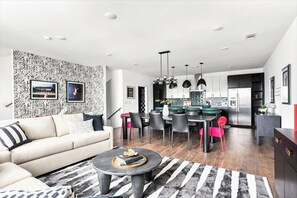 Un salon moderne avec un canapé, une table basse et un mur décoré d’un motif. On aperçoit à l’arrière-plan un coin repas avec des chaises et une table.