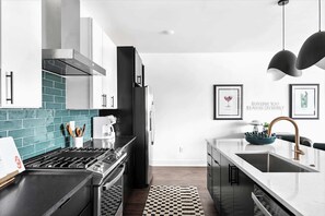 Une cuisine moderne avec un four noir, des appareils en acier inoxydable et un plan de travail blanc.