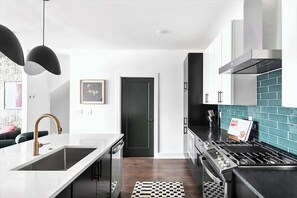 A modern kitchen with a central island, stainless steel appliances, and a black door. - Fall getaway: hot tub house sleeps 10 near Germantown, Nashville (Nashville)