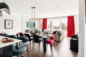 A modern living room with a dining area, featuring a sofa, chairs, a table with a wine glass, and a red curtain.