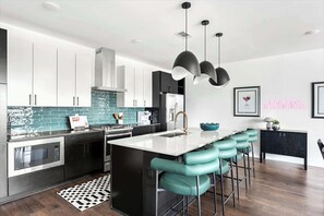A modern kitchen with a central island, bar stools, stainless steel appliances, and pendant lighting.