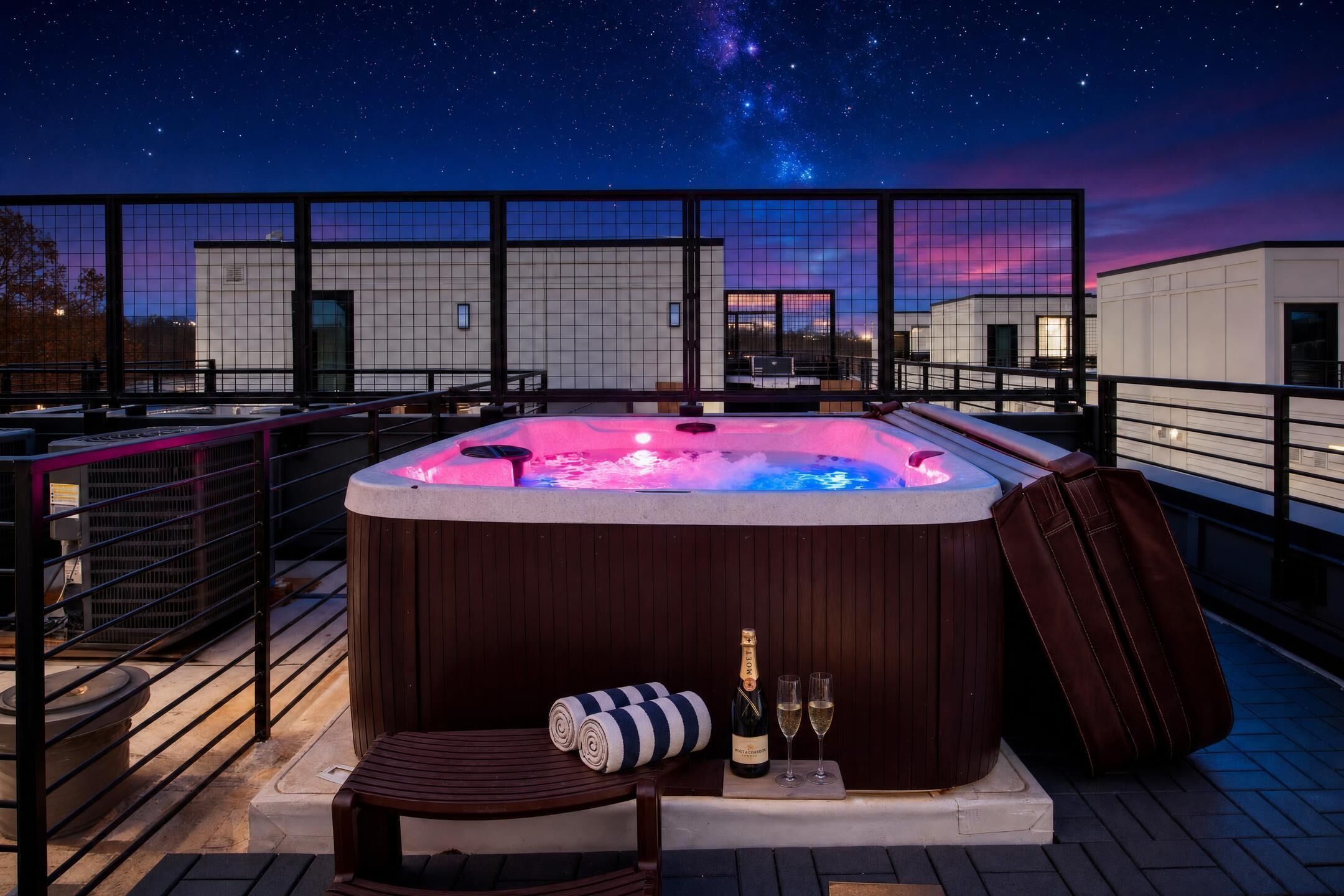 A hot tub on a rooftop terrace with a night sky view, a bottle of champagne, and a striped towel.