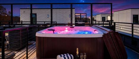 Un bain à remous sur une terrasse en toit-terrasse offrant une vue sur le ciel nocturne, une bouteille de champagne et une serviette à rayures.