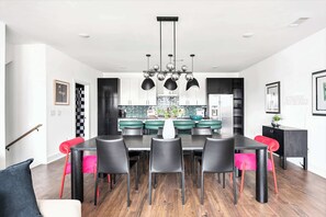 A modern dining area with a black and white color scheme, featuring a central island, black chairs, and a unique chandelier.