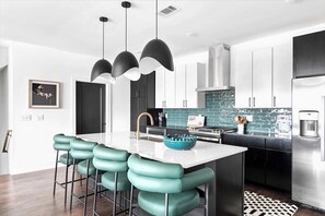 A modern kitchen with a central island, bar stools, pendant lighting, and stainless steel appliances.