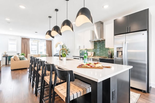 A modern kitchen with a central island, bar stools, stainless steel appliances, and pendant lighting.