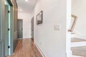 A hallway with wooden flooring, a staircase with wooden steps, and a door with a light switch.