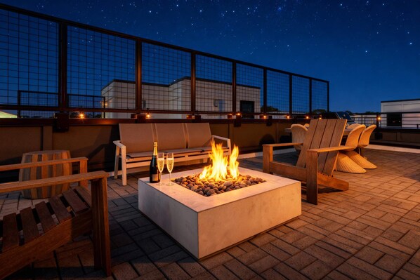 A rooftop terrace with a fire pit, seating, and a view of the night sky.