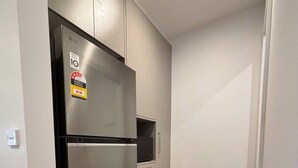 Una cocina compacta con un refrigerador de acero inoxidable, un microondas y un horno empotrado. La cocina tiene paredes de colores claros y piso de madera.