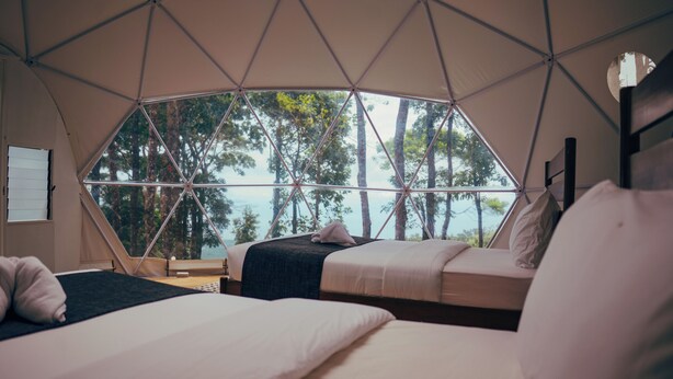 A tented accommodation with two beds, a view of trees and water, and a simple interior design. - Matahom Forest Glamping Tent 2 (Mambajao)