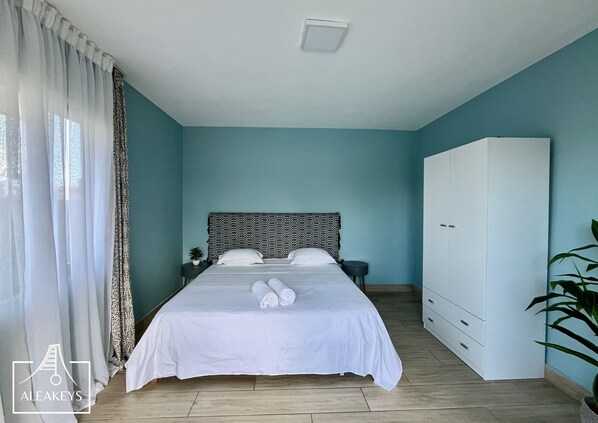 A bedroom with a bed, a wardrobe, a nightstand, and a potted plant.