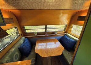 A cozy interior with a wooden table and bench seating, a window with a view, and a patterned ceiling.