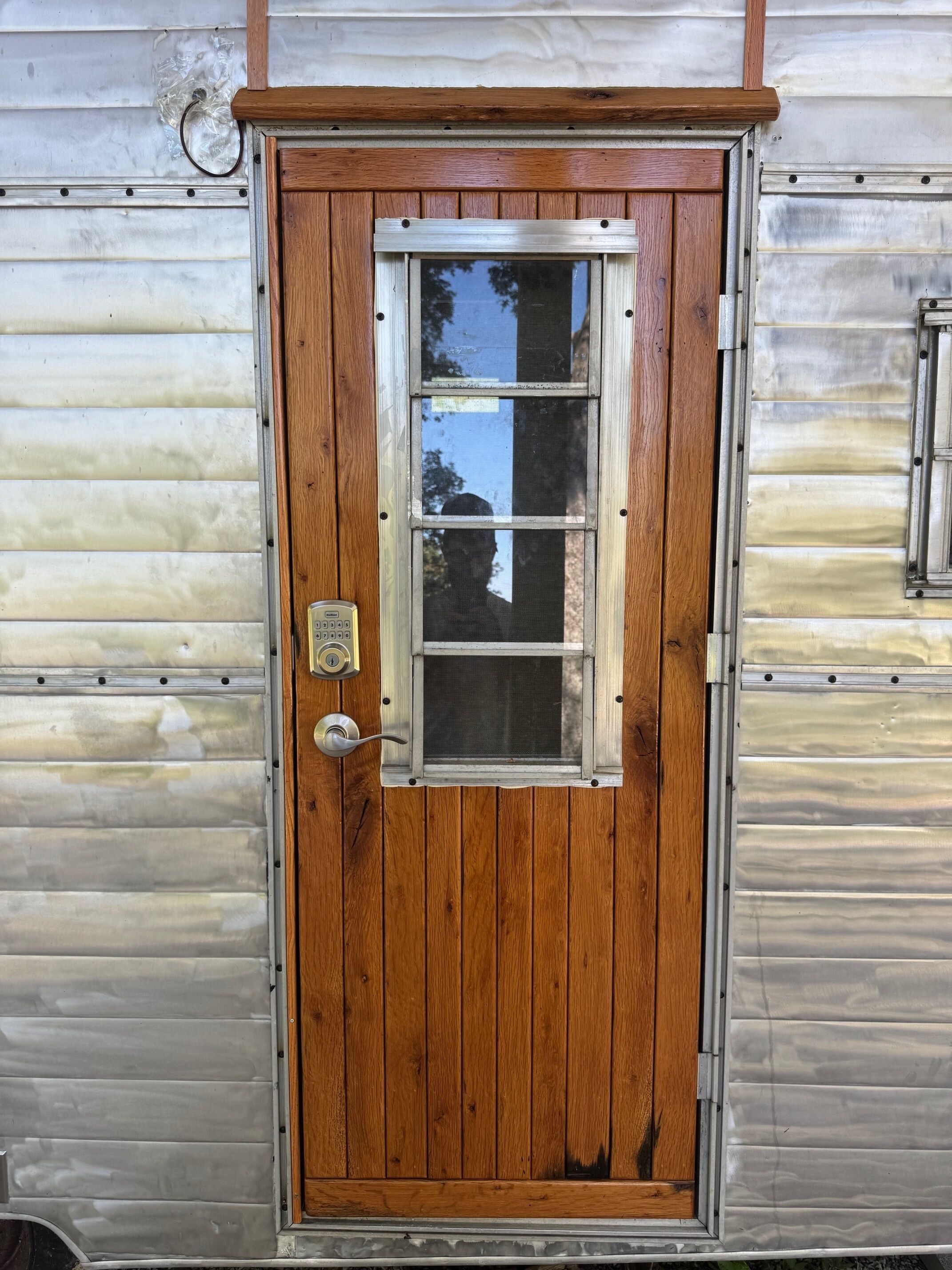 A wooden door with a window, a doorbell, and a mail slot.