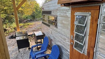 Un espacio al aire libre techado con una parrilla, sillas azules y una puerta de madera.