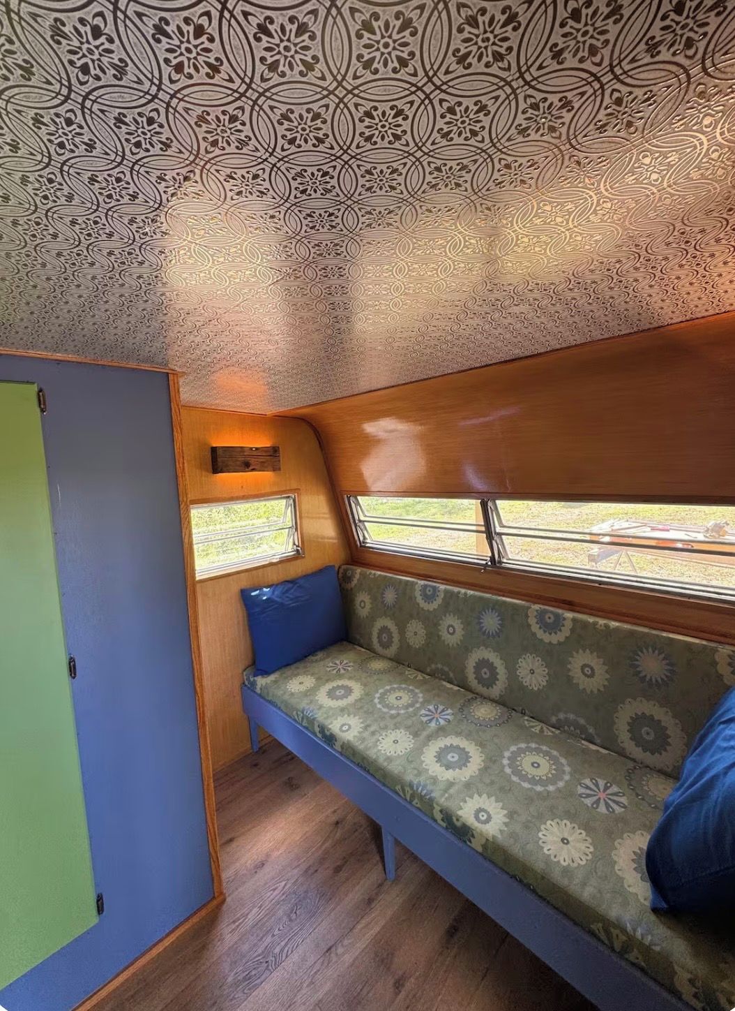Un intérieur compact avec un plafond orné de motifs, un banc agrémenté de coussins et une fenêtre offrant une vue sur l’extérieur.