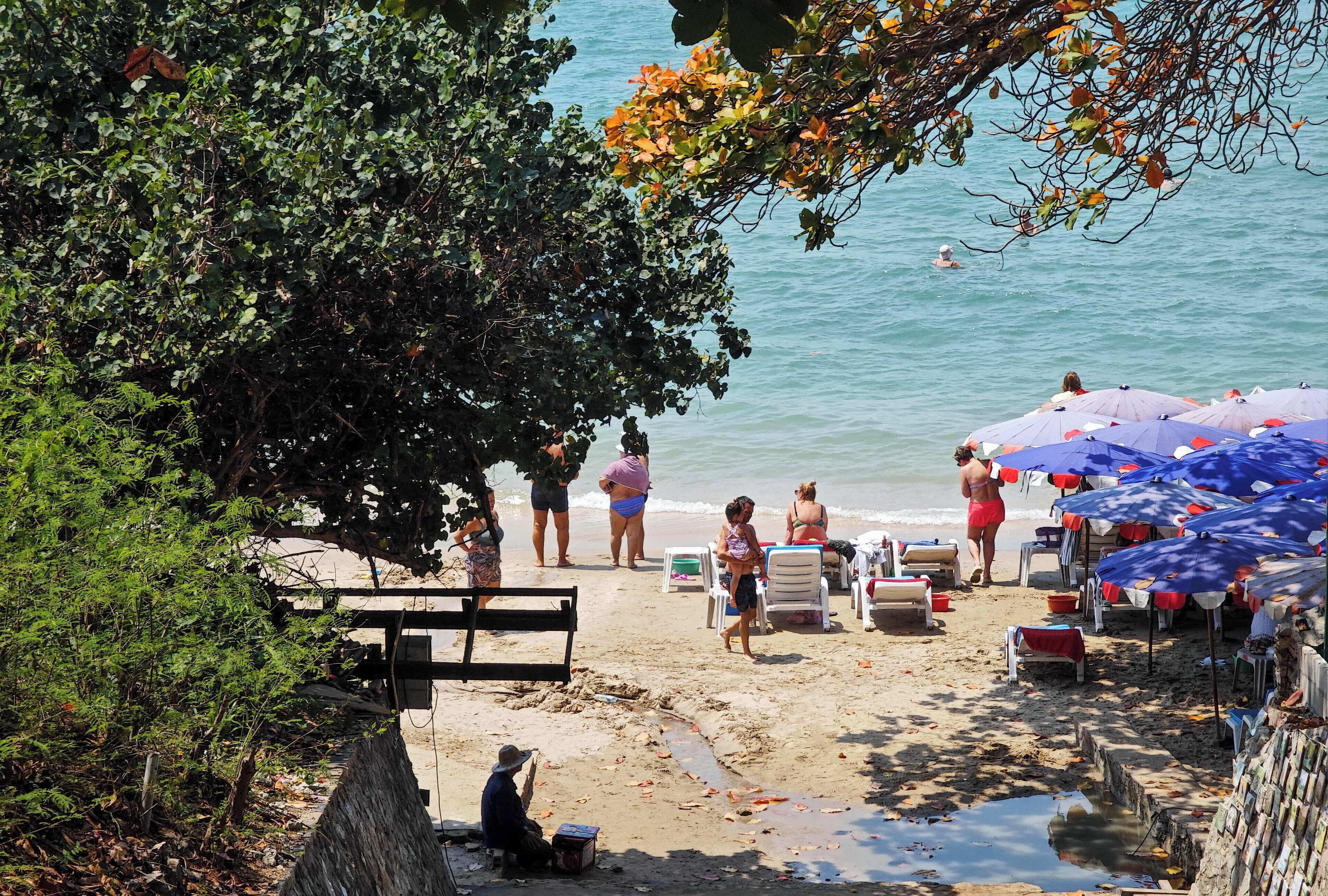 A beach with umbrellas, chairs, and people.