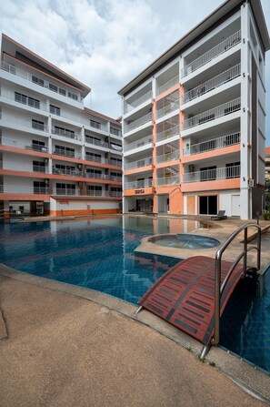 Un hotel de varios pisos con piscina, balcones y una zona cubierta.