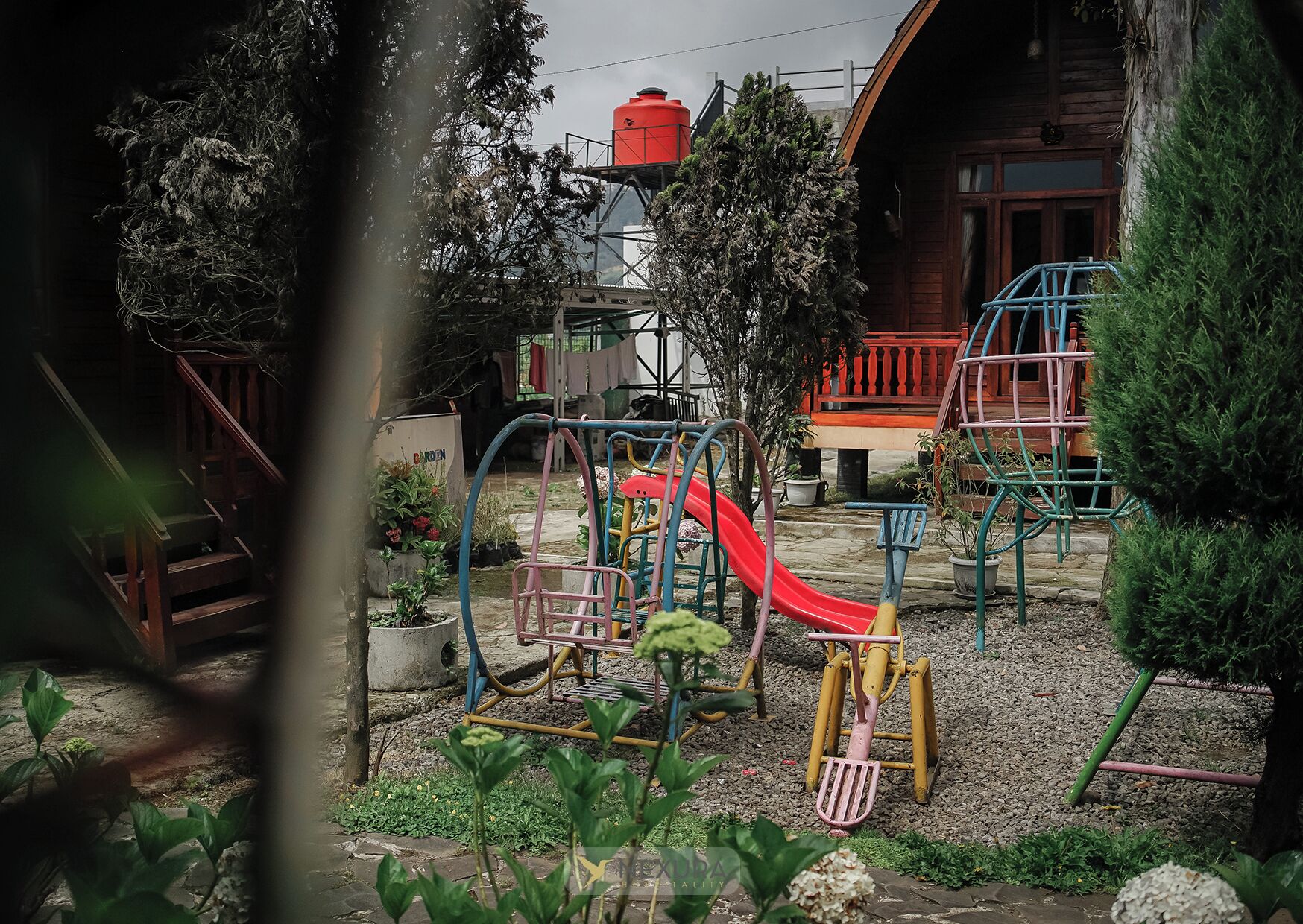 Un parque infantil con tobogán y estructuras para escalar, rodeado de plantas en macetas y una valla de madera.