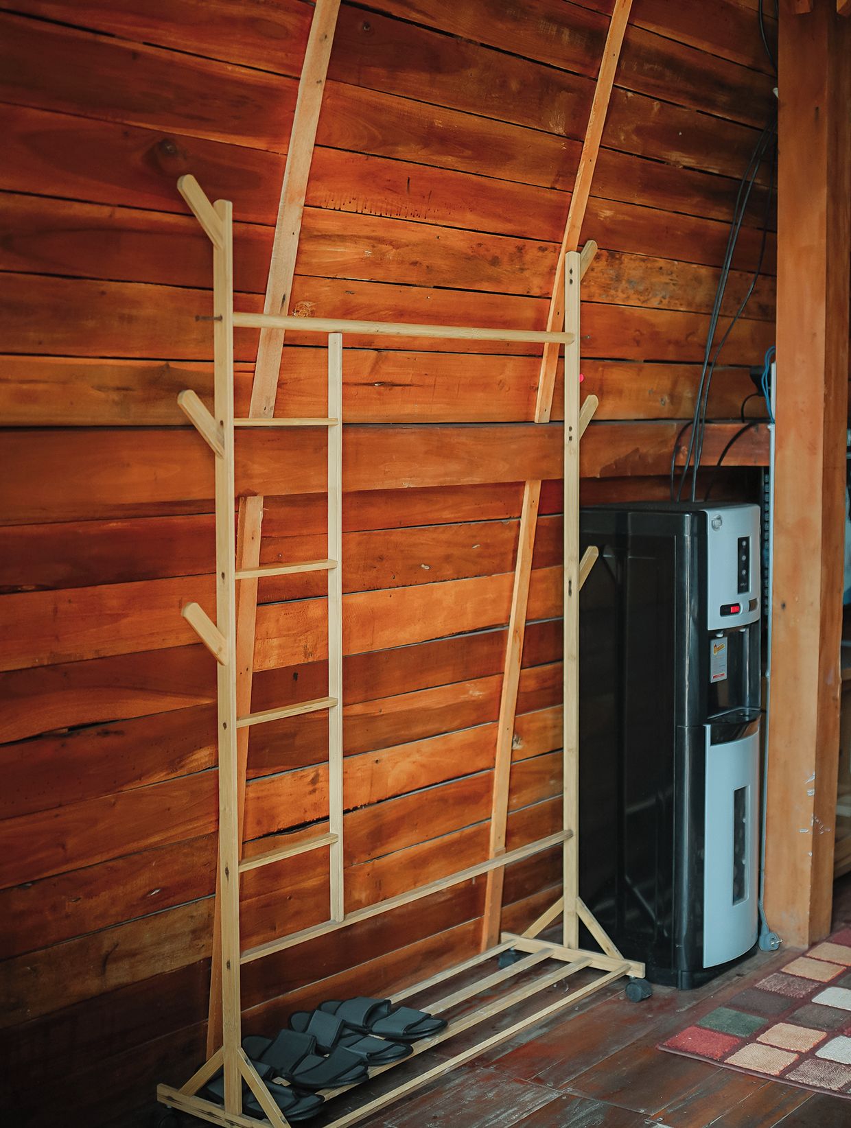 A wooden ladder rack against a wooden wall, with a water dispenser and a small table with shoes underneath.