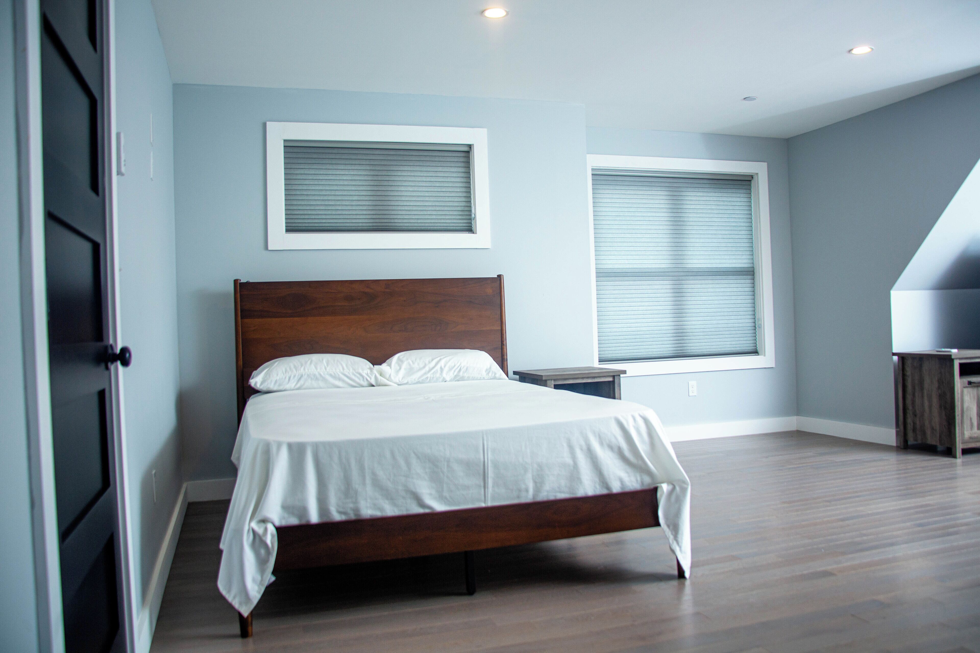 Un dormitorio con una cama de madera, dos mesitas de noche y dos ventanas con persianas.
