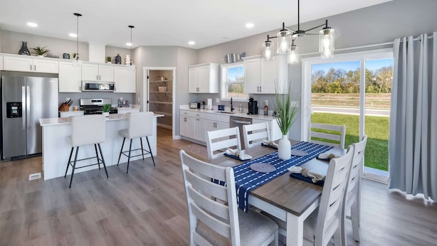 Cocina moderna con muebles blancos, un refrigerador de acero inoxidable y un comedor con mesa de madera y sillas blancas.