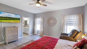 A bedroom with a bed, a chair, a TV, a ceiling fan, and a view of a field. - Harbor Village Neighborhood at Heritage Harbor (Ottawa)