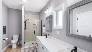 A modern bathroom with a glass shower enclosure, a white toilet, a vanity with a mirror, and a light fixture above the mirror. - Harbor Village Neighborhood at Heritage Harbor (Ottawa)