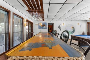 A long dining table with a rope edge, surrounded by chairs, in a room with a high ceiling and wooden beams. - Parrothead Retreat - Steinhatchee (Steinhatchee)