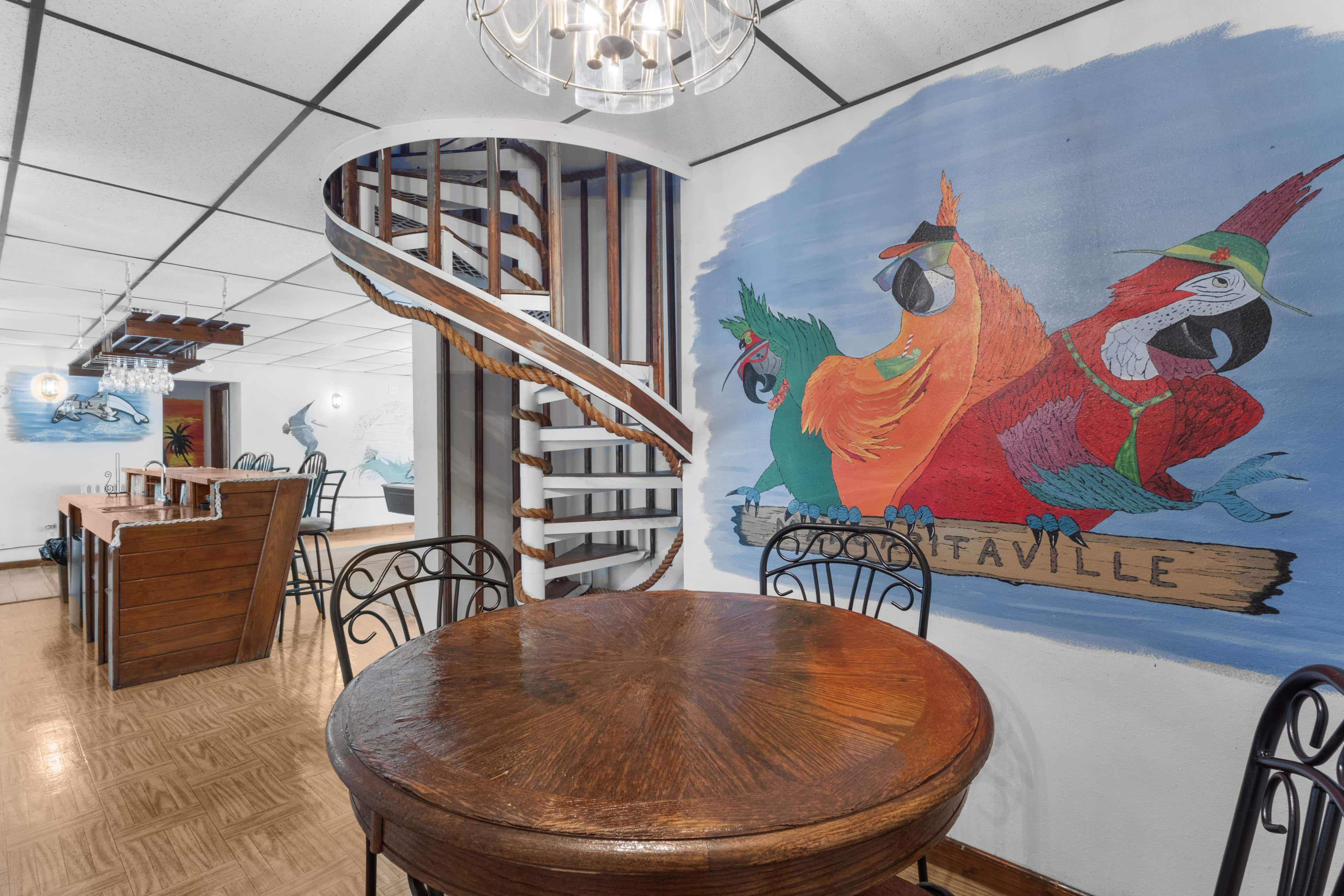 A dining area with a wooden table and chairs, a spiral staircase, and a mural on the wall.